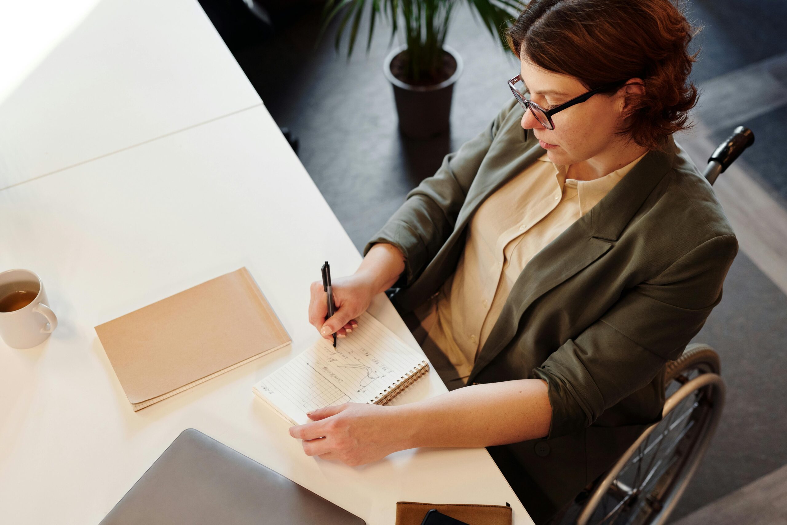 Woman in wheelchair sitting at an office desk with a piece of paper